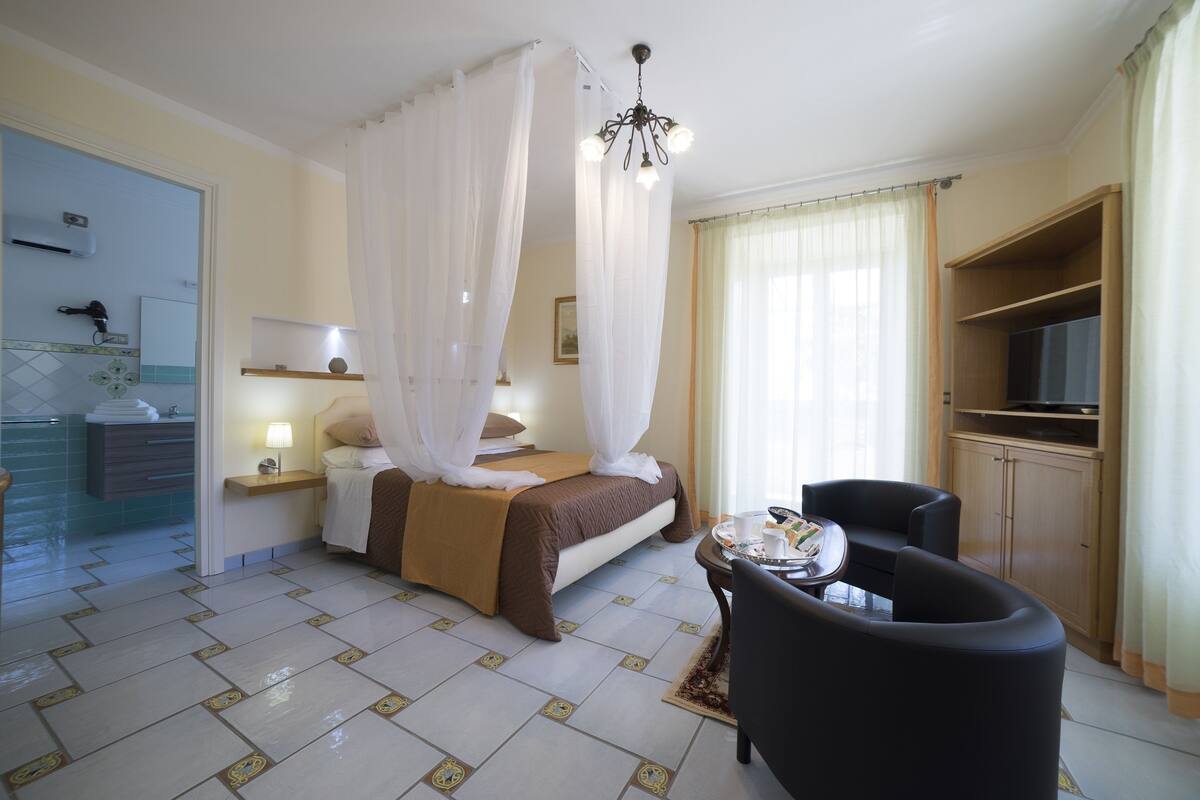 A hotel room with a bed, a desk, a chair, a TV, and a bathroom visible through an open door.