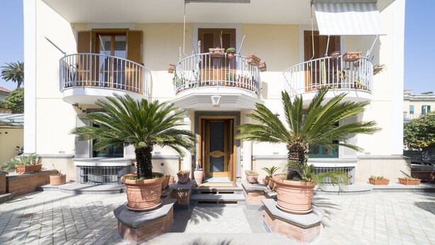 Un bâtiment doté d’une entrée centrale, de deux balcons avec des garde-corps et de plantes en pot devant.