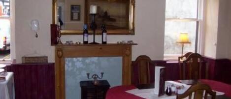 A room with a wooden fireplace, a table with a red tablecloth, and a mirror above the fireplace.