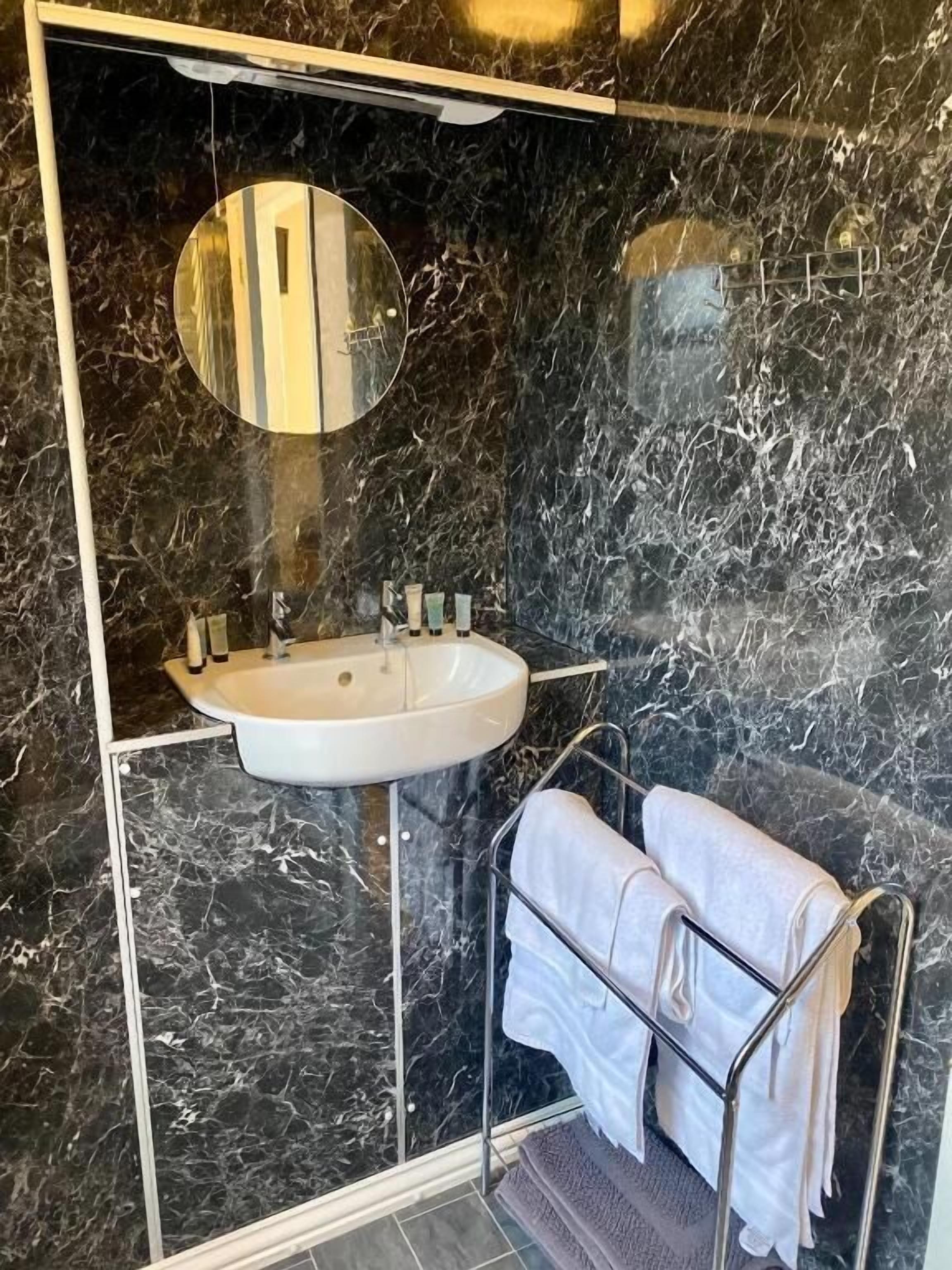 A bathroom with a marble wall, a sink, a mirror, and a towel rack.