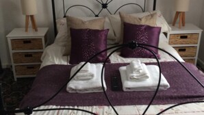 A neatly made bed with a metal frame, two bedside tables with lamps, a painting on the wall, and a small wooden cabinet.