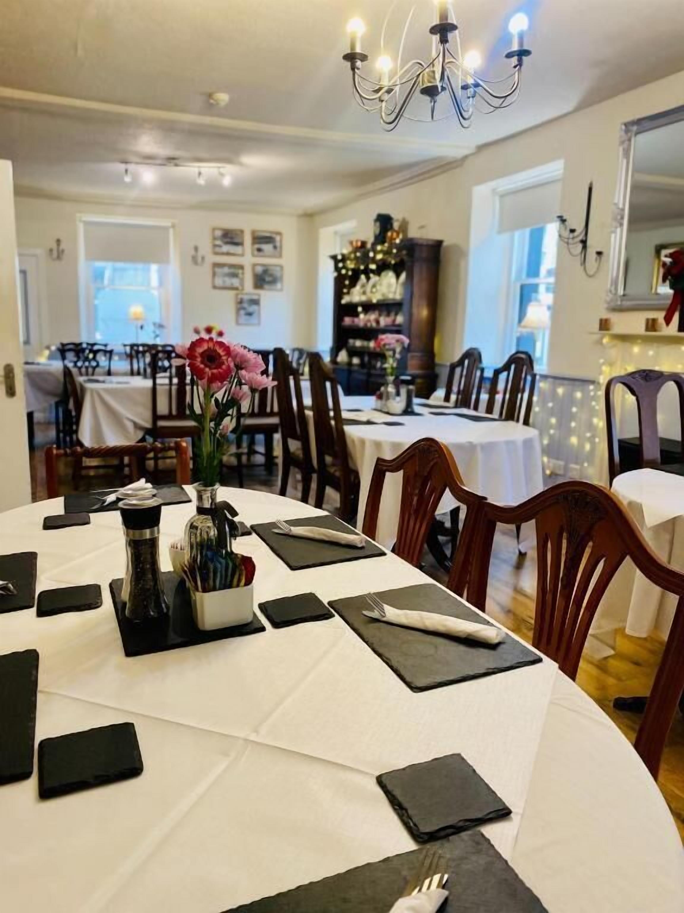 Un espace repas avec des tables rondes dressées pour le dîner, un lustre et un sapin de Noël en arrière-plan.