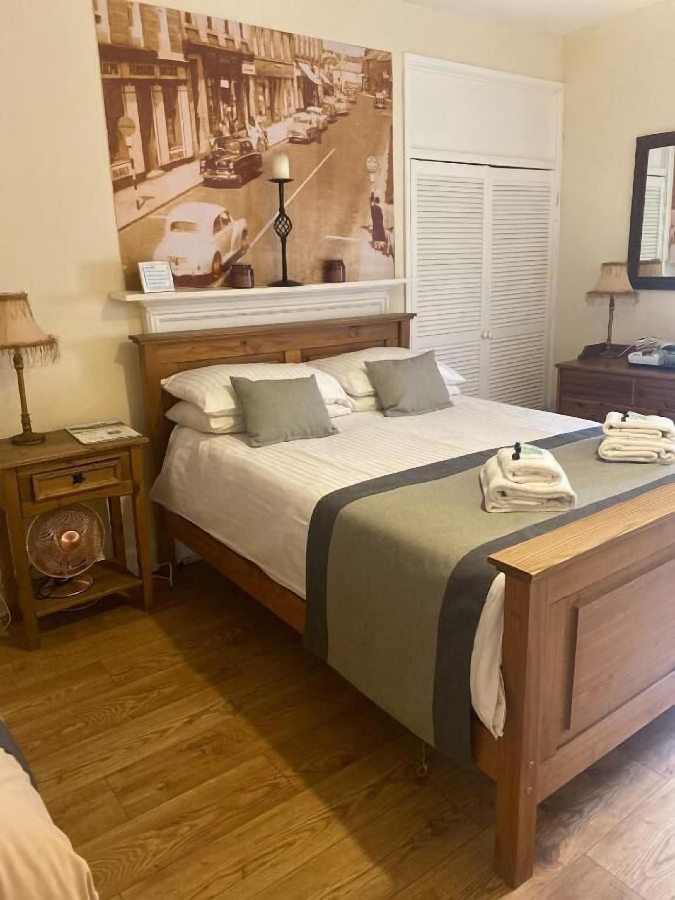 A hotel room with a bed, a nightstand, a lamp, a mirror, and a window with blinds.