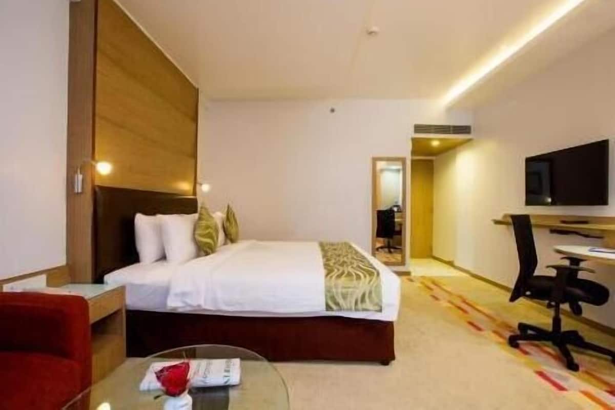 Quarto de hotel com cama, escrivaninha, cadeira e televisão.