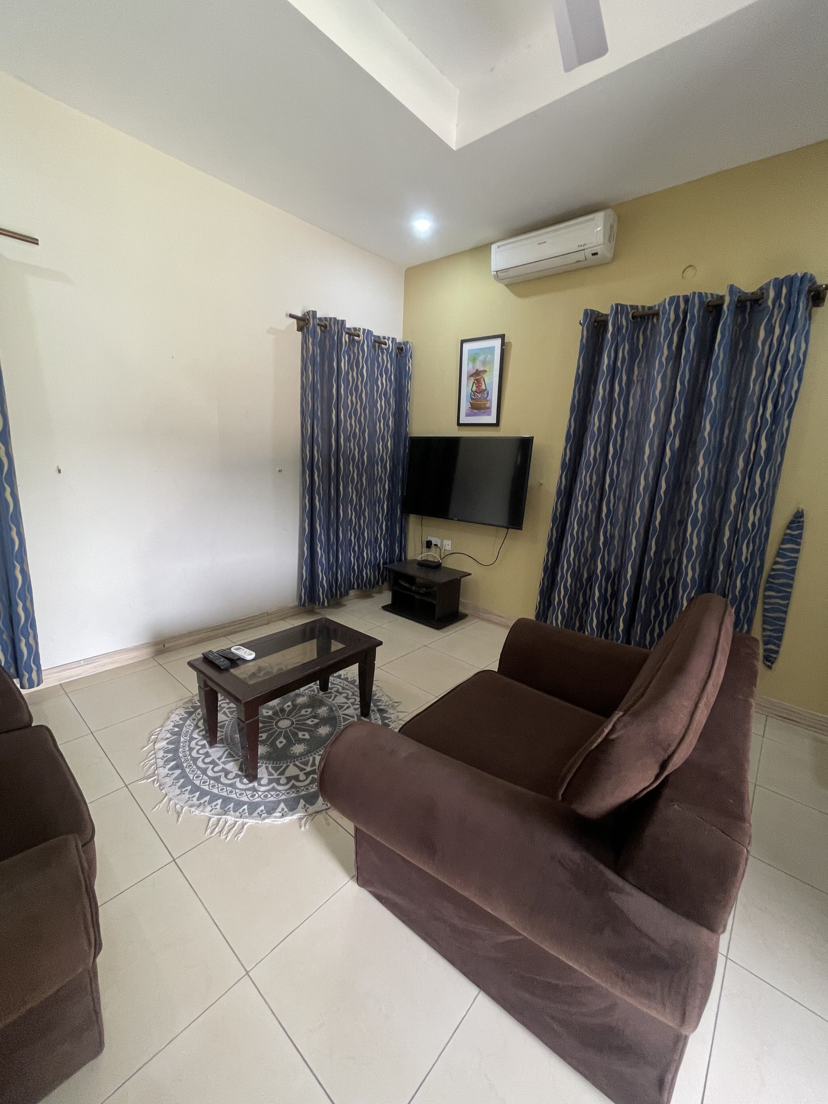 A living room with a brown sofa, a coffee table, a TV, and patterned curtains.