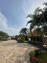 Um pátio pavimentado com piso de pedra, rodeado por palmeiras e sebes bem cuidadas.