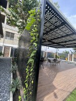 Área de pátio com pergolado, assentos e plantas.