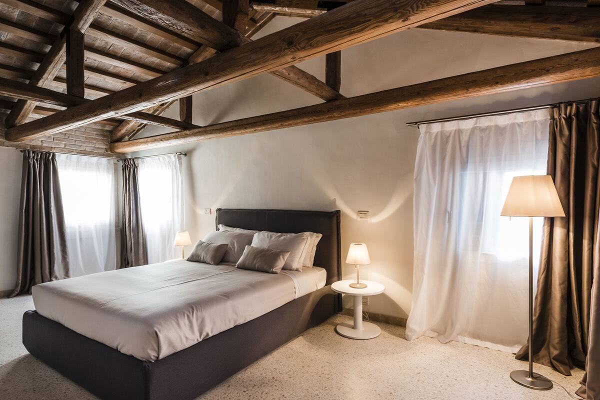 Quarto com uma cama grande, duas luminárias de cabeceira e teto de madeira.