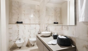 A modern bathroom with a marble backsplash, a large mirror, a sink, a bidet, and a towel rack. - MYSWEETPLACE - San Marco Apartments (Venice)
