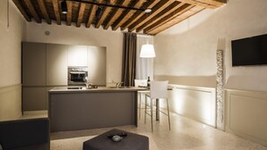 A modern kitchen with a central island, a dining area with a bar stool, and a flat-screen TV mounted on the wall. - MYSWEETPLACE - San Marco Apartments (Venice)