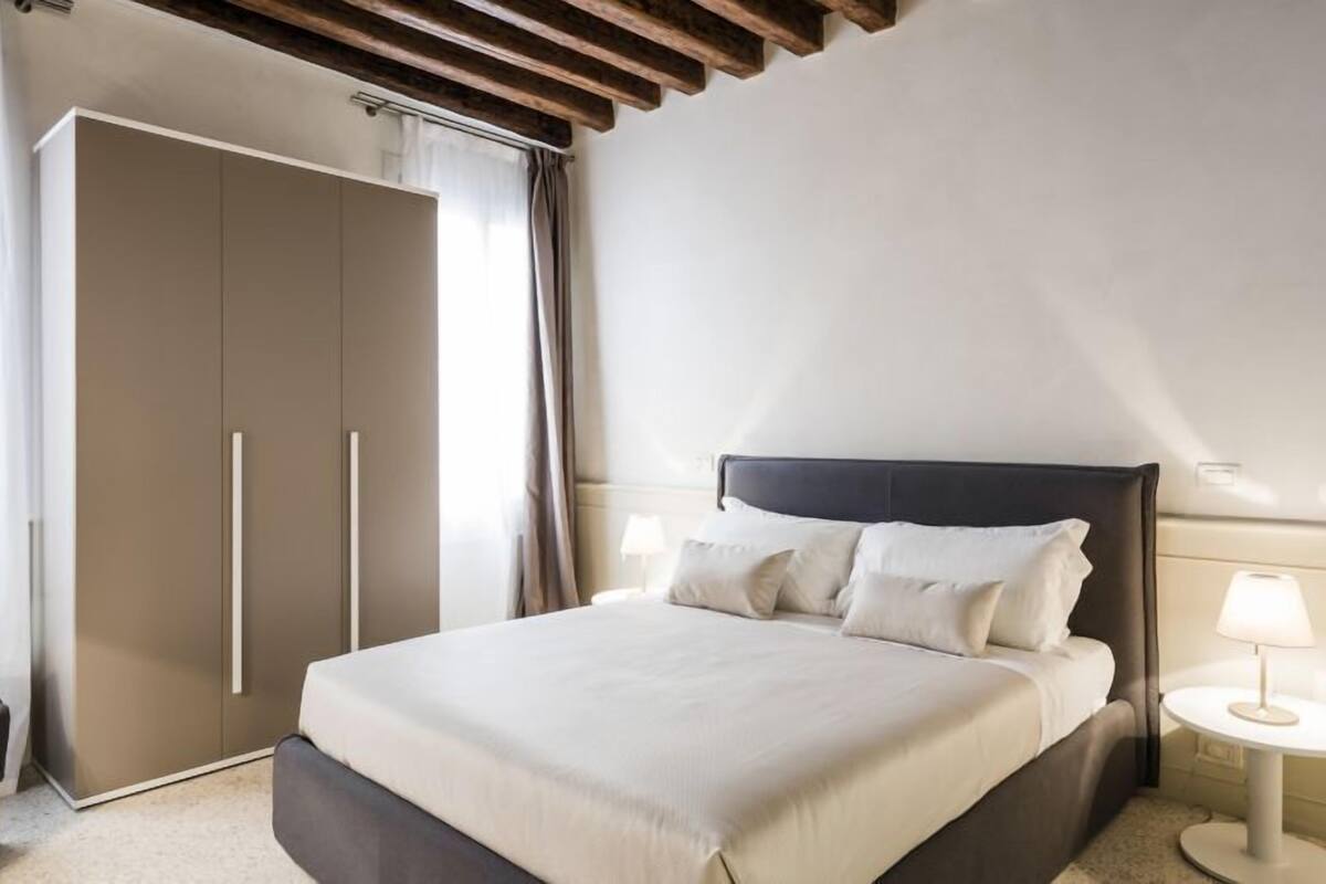 Quarto moderno com uma cama grande, um guarda-roupa, uma mesa de cabeceira com abajur e uma cadeira.