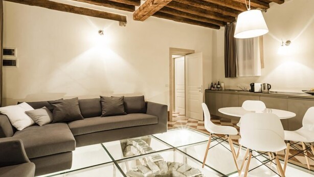 A modern living room with a sofa, a glass coffee table, and a dining area with chairs and a table. - MYSWEETPLACE - San Marco Apartments (Venice)