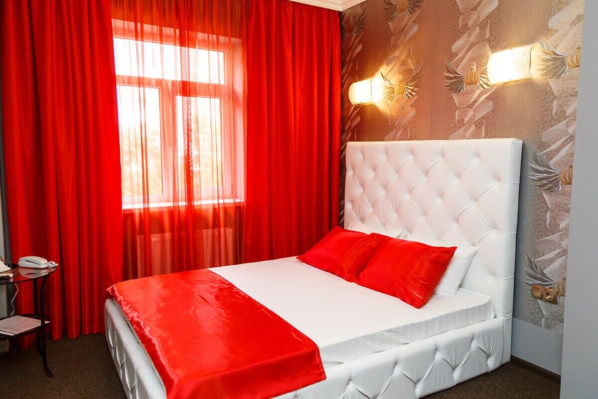 Une chambre d’hôtel avec un lit blanc, des rideaux rouges et un luminaire fixé au mur.