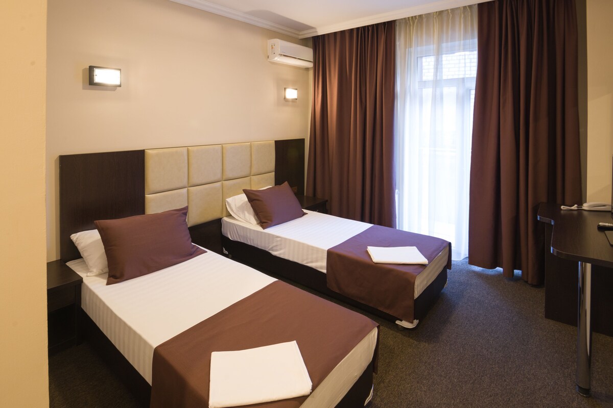 Une chambre d’hôtel avec deux lits simples, un bureau et une fenêtre avec des rideaux.