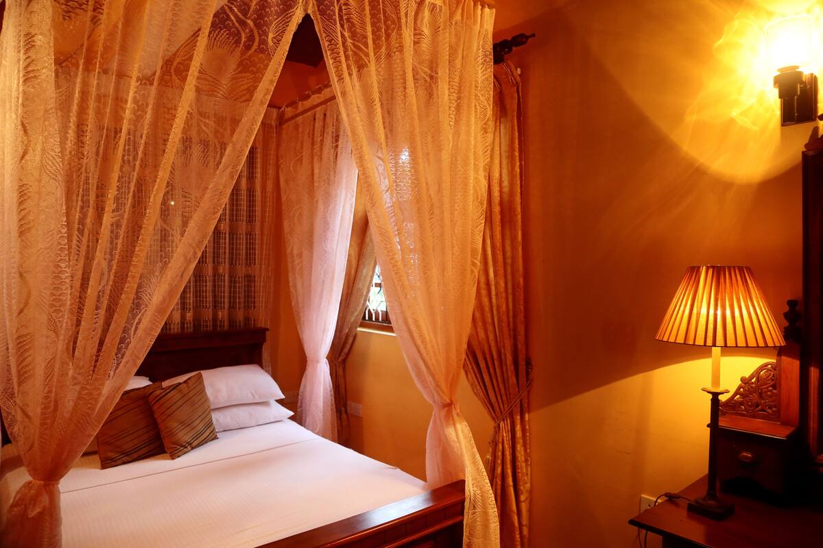 A bed with a canopy, a bedside lamp, and a window with curtains.