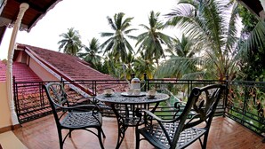 A balcony with a table and chairs, overlooking palm trees and a red-roofed building. - The Castle (Seeduwa - Katunayake)