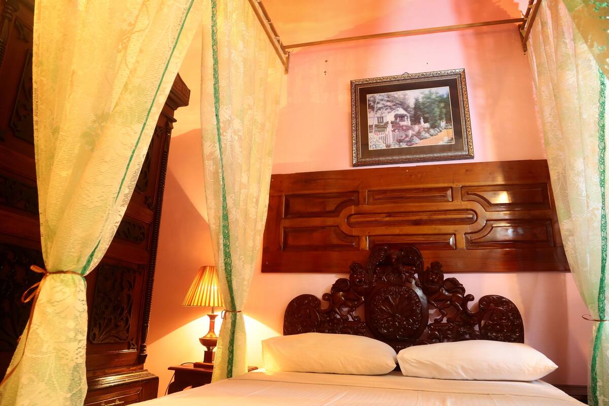 A room with a bed, a wooden headboard, a framed picture on the wall, and a nightstand with a lamp.