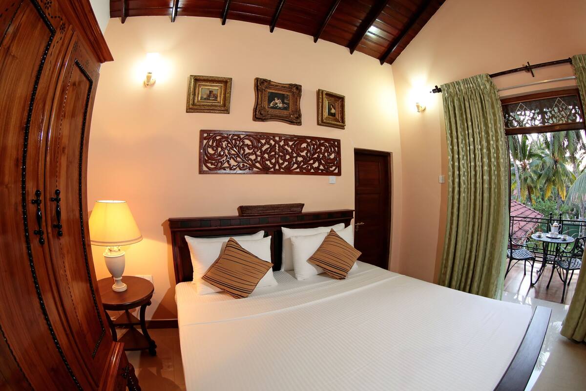 A hotel room with a bed, a nightstand, a lamp, a decorative wall panel, and a view of the outdoors.