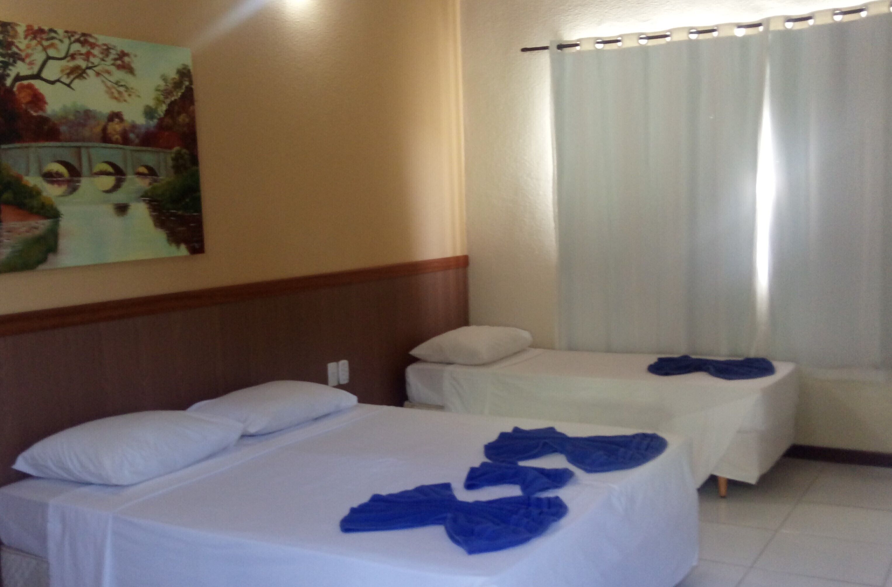 A hotel room with two beds, a painting on the wall, and a window with curtains.