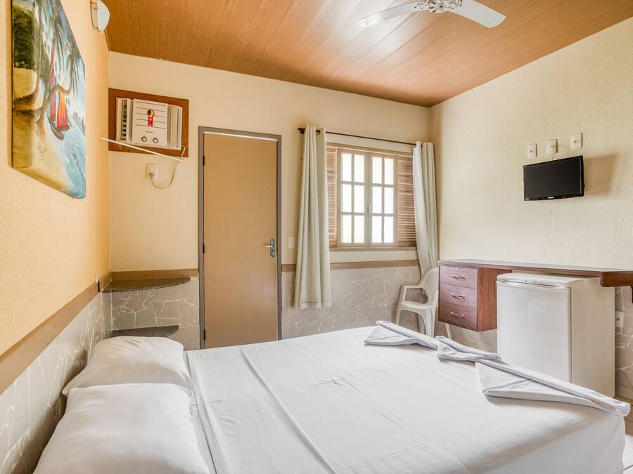 Ein Hotelzimmer mit einem Bett, einem kleinen Schreibtisch, einem Fernseher und einem Fenster mit Vorhängen.