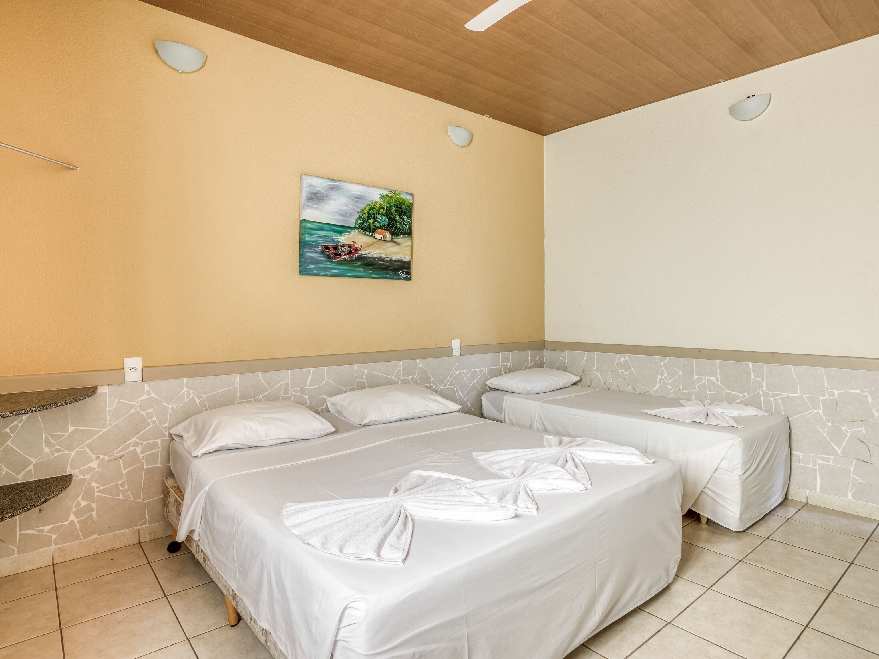 A hotel room with two beds, a painting of a beach scene, and a ceiling fan.