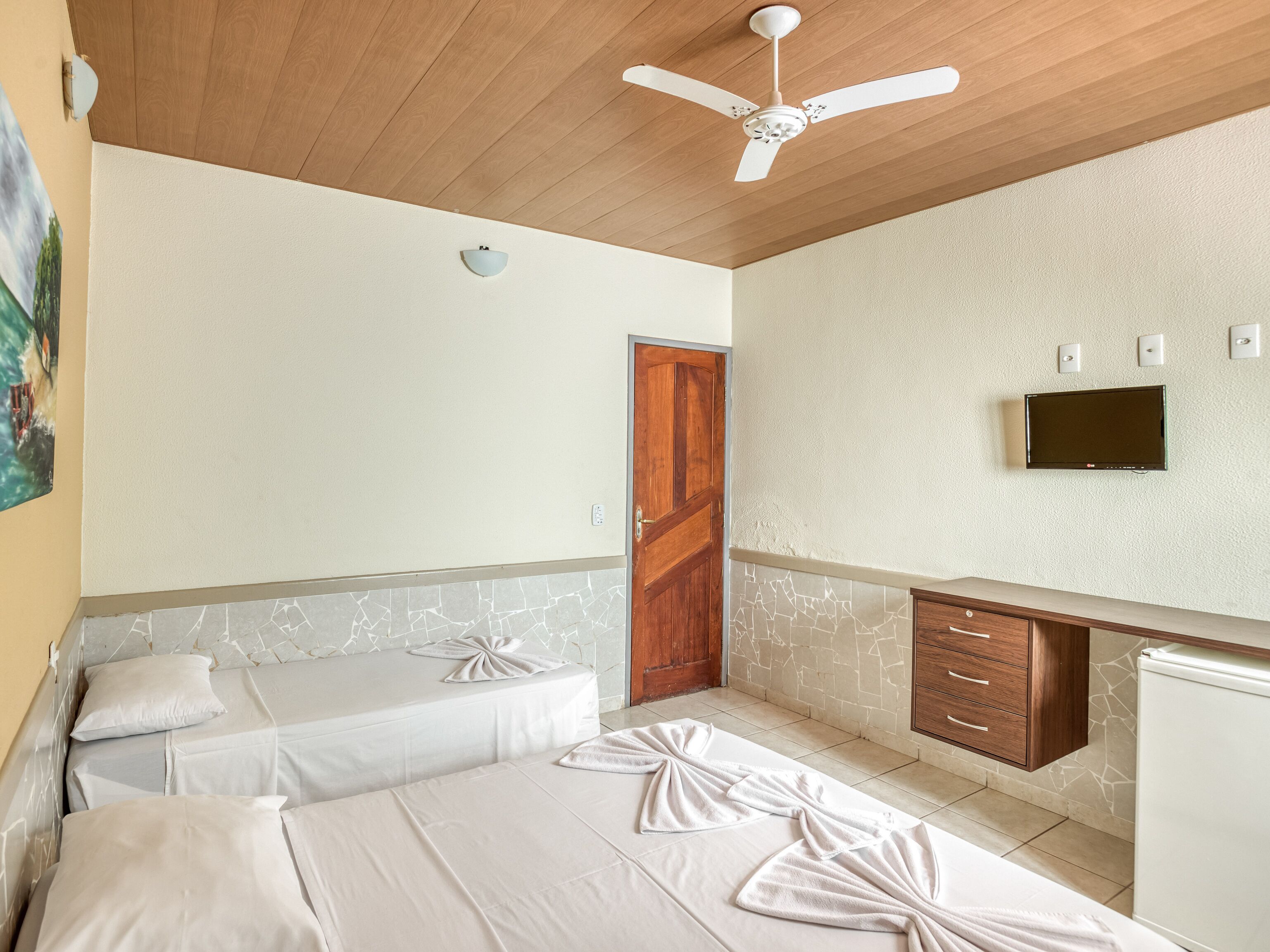 Habitación de hotel con dos camas, ventilador de techo, televisión y armario de madera.