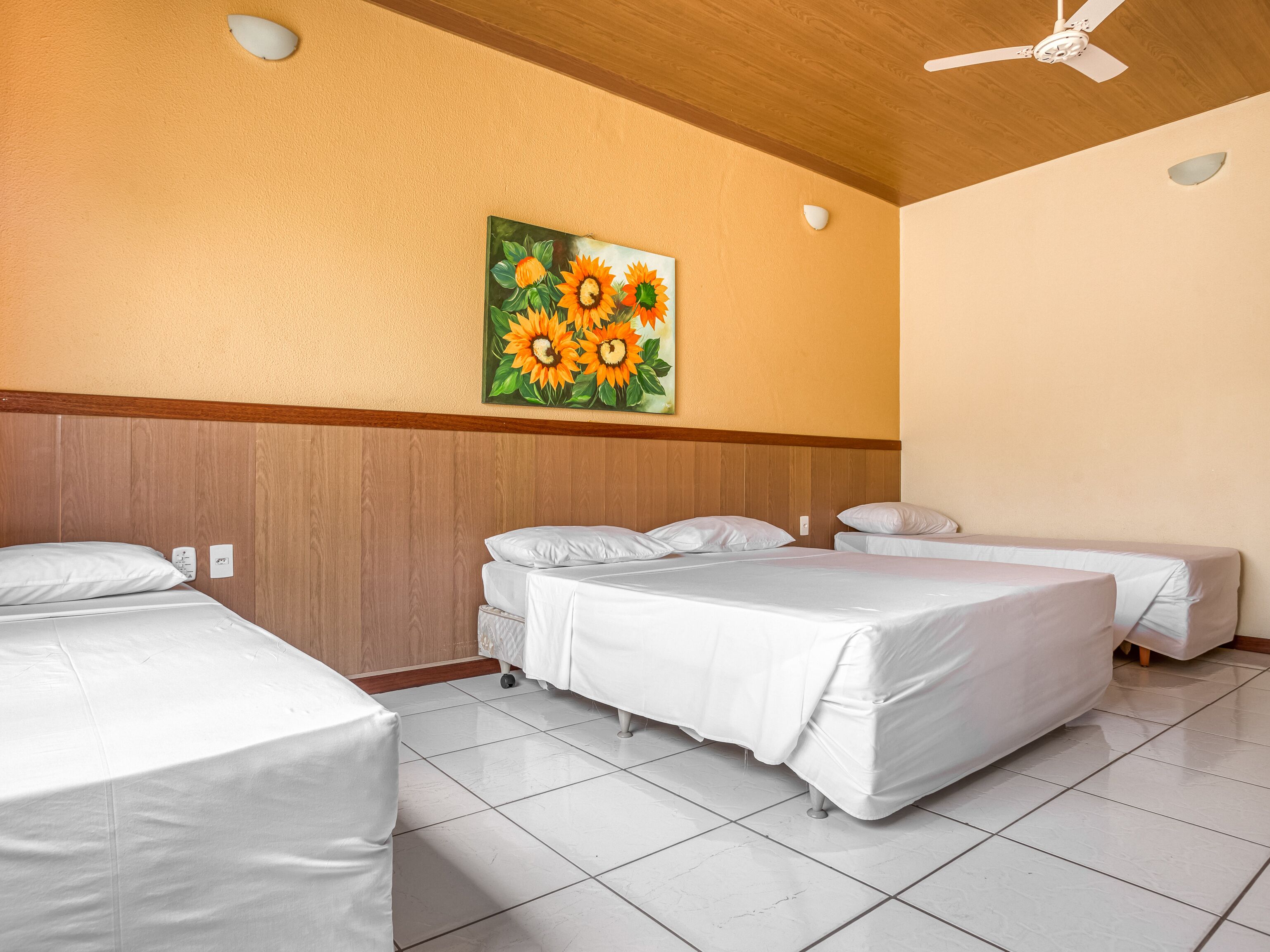 A hotel room with two beds, a ceiling fan, and a painting of sunflowers on the wall.