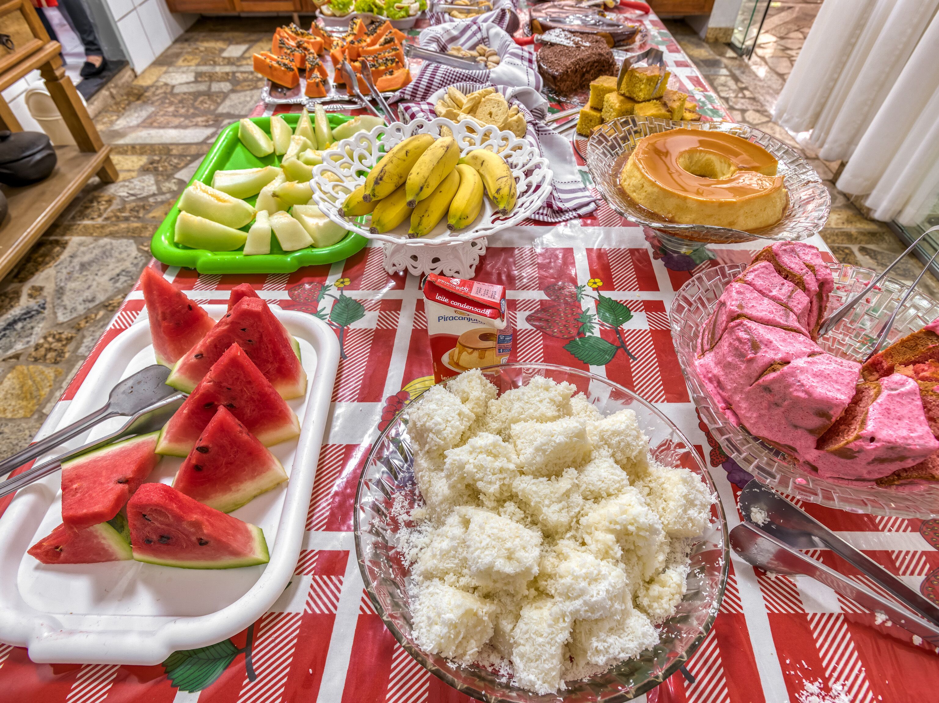 Una mesa de buffet con distintos alimentos, incluyendo sandía, plátanos y un pastel.