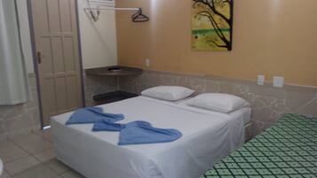 Una habitación de hotel pequeña con cama, mesita de noche, toalla, un cuadro en la pared y alfombra estampada.