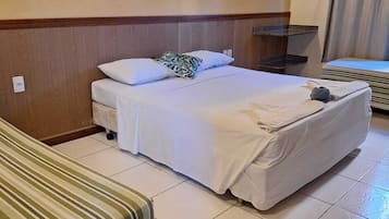Habitación de hotel con cama, mesita de noche, lámpara colgante, zona de ducha y colcha a rayas.