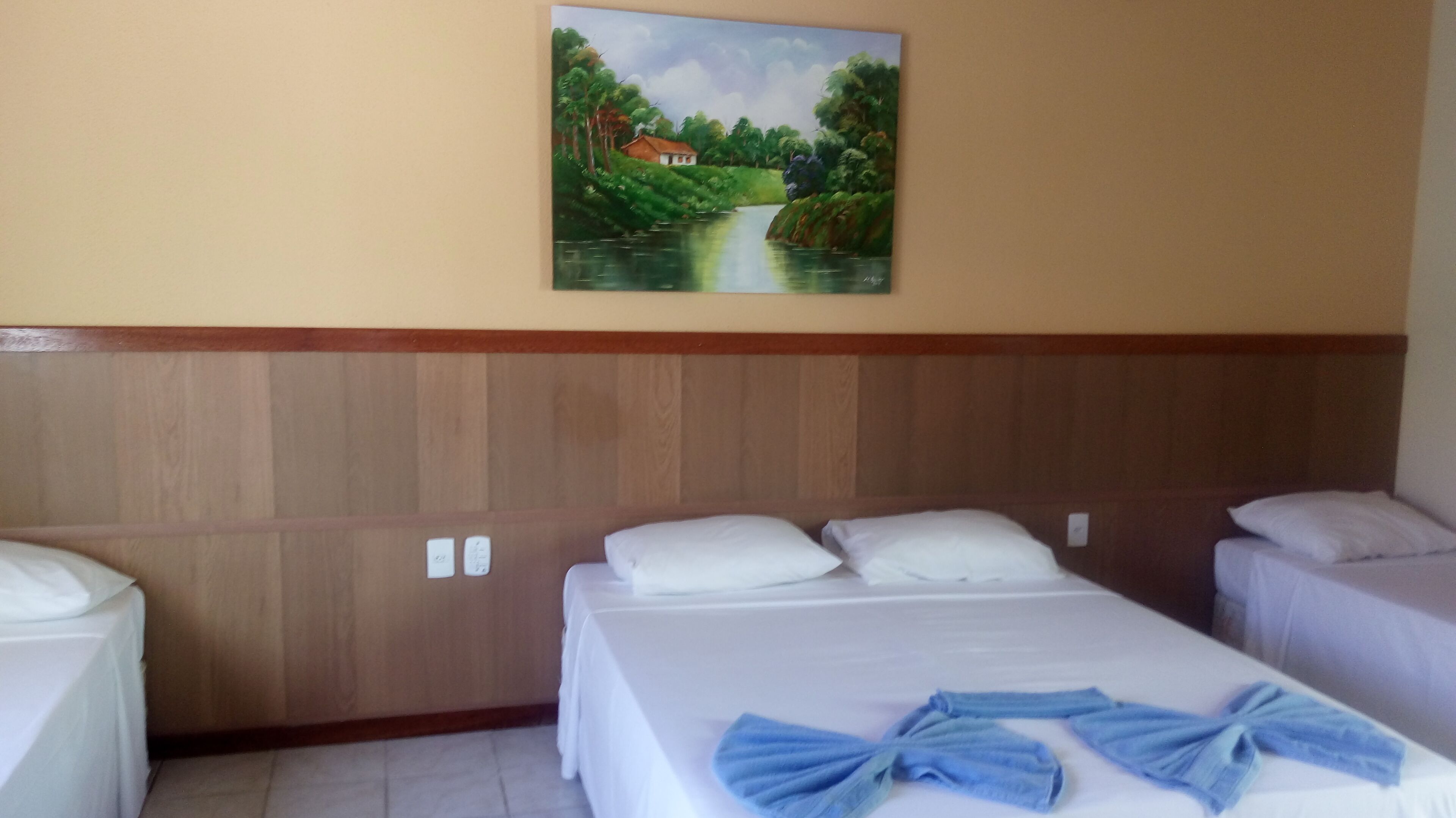 A hotel room with two beds, a wooden headboard, a painting of a landscape, and a blue towel on the bed.