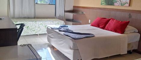 A hotel room with two beds, a desk, a refrigerator, and a window with curtains.
