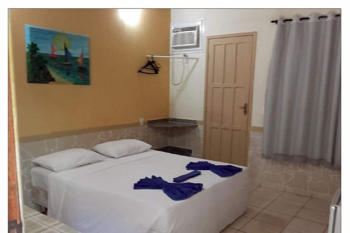 Habitación de hotel con cama, un cuadro en la pared, zona de ducha y una puerta.