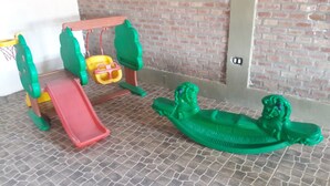 A children's play area with a slide, swings, and a green toy dinosaur. - Complejo Rumipal (Villa Rumipal)