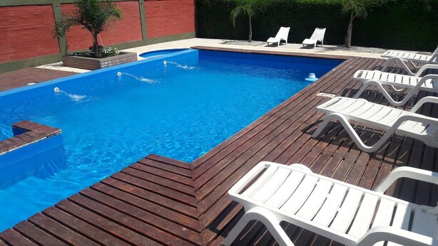 A swimming pool with wooden deck and white lounge chairs. - Complejo Rumipal (Villa Rumipal)