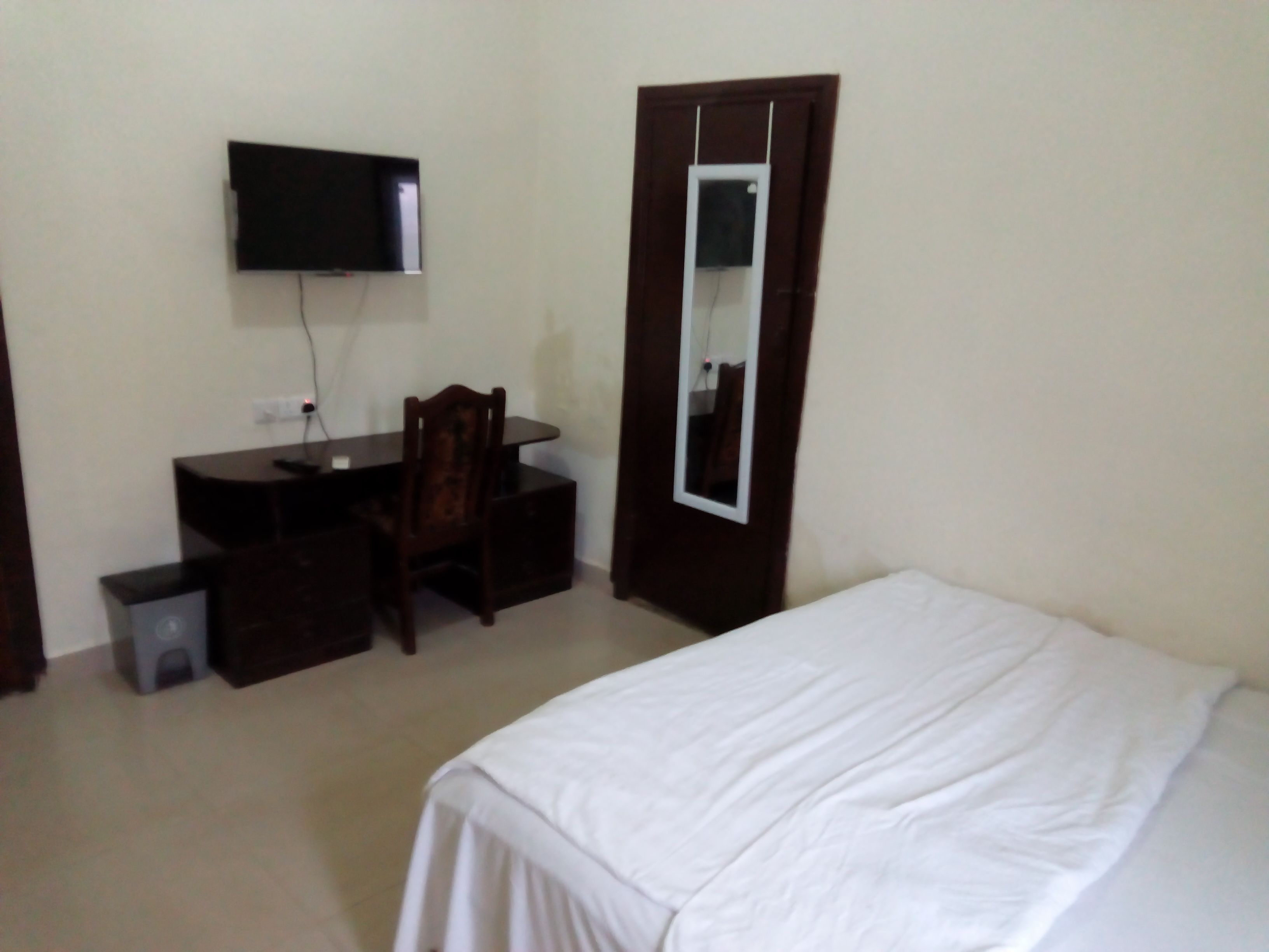 Une chambre à coucher comprenant un lit, un bureau avec une chaise, un téléviseur fixé au mur et un miroir sur la porte.