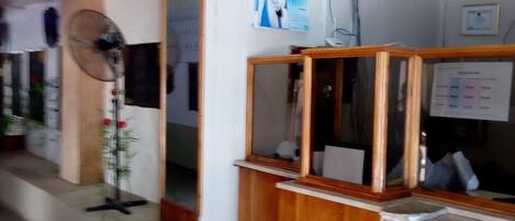 Una recepción con mostrador de madera, un ventilador de pared y un cartel con texto e imágenes.