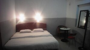 Habitación de hotel con cama, dos lámparas de noche, una mesita con silla y un espejo en la pared.