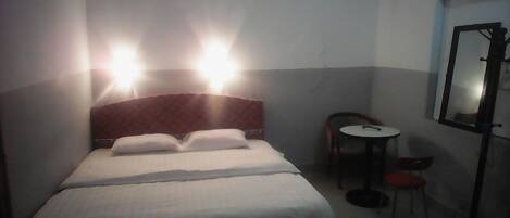 Una camera d'albergo con un letto, due lampade ai comodini, un tavolino con una sedia e uno specchio a parete.
