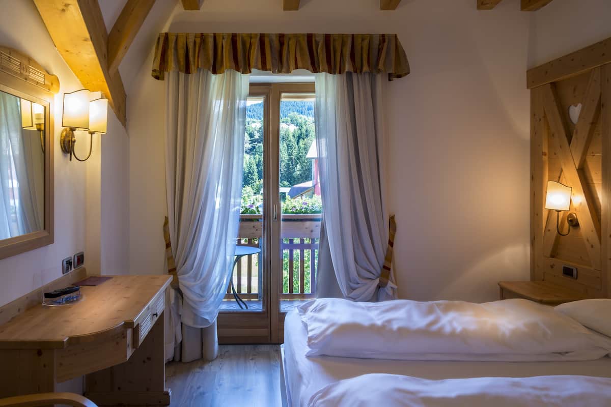 A bedroom with a wooden desk, a bed, and a balcony with curtains.