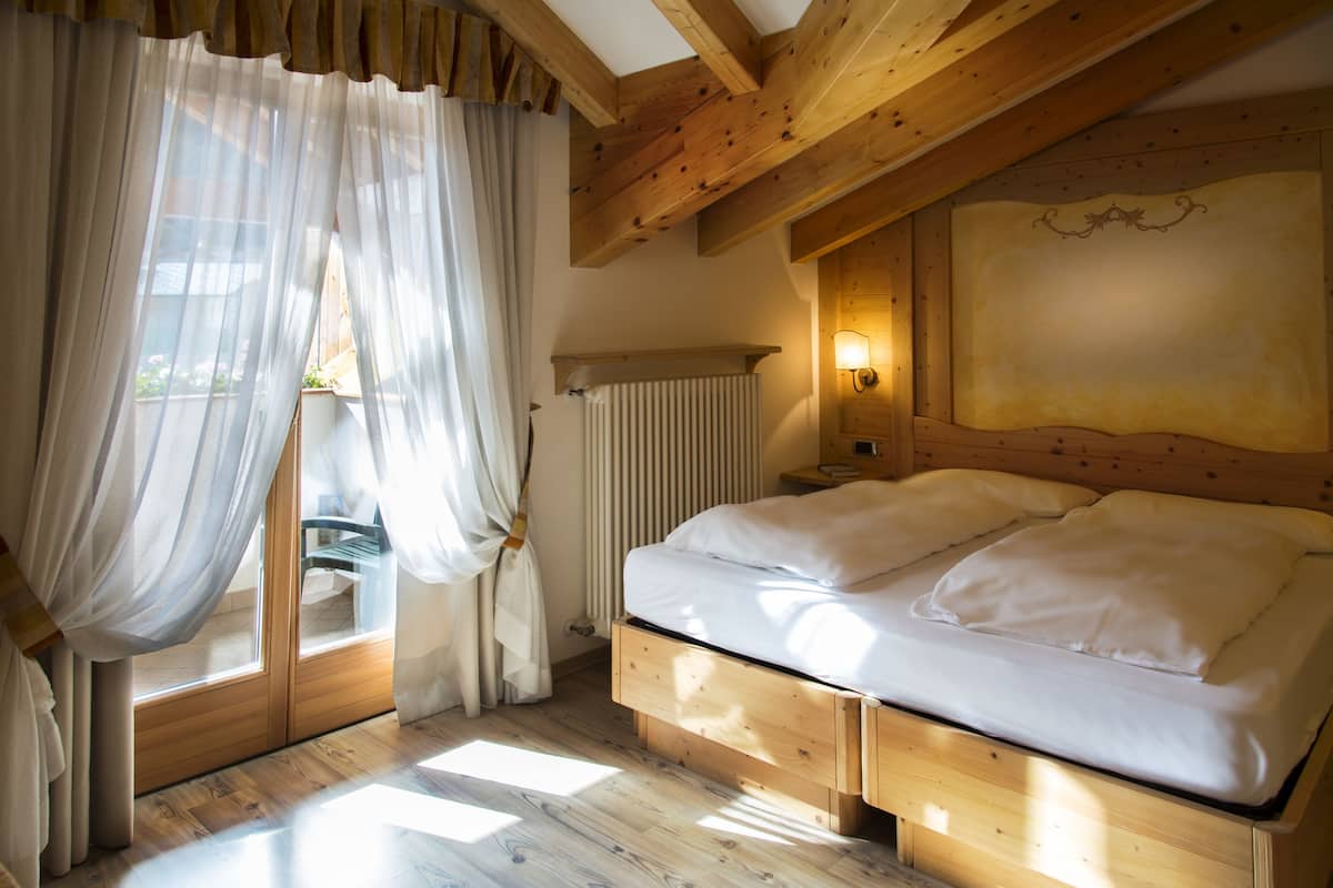 A bedroom with a wooden bed, a window with sheer curtains, and a radiator.