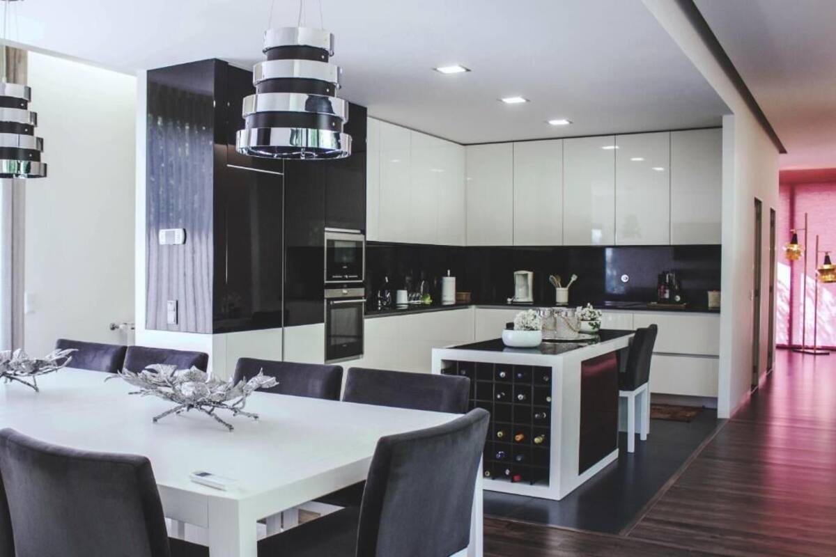 Une cuisine moderne avec des meubles blancs, un îlot central et un coin repas comprenant une table blanche et des chaises noires.