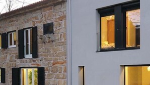 Un edificio moderno de dos pisos con paredes de piedra y contraventanas negras, con ventanas amplias y un césped bien cuidado.
