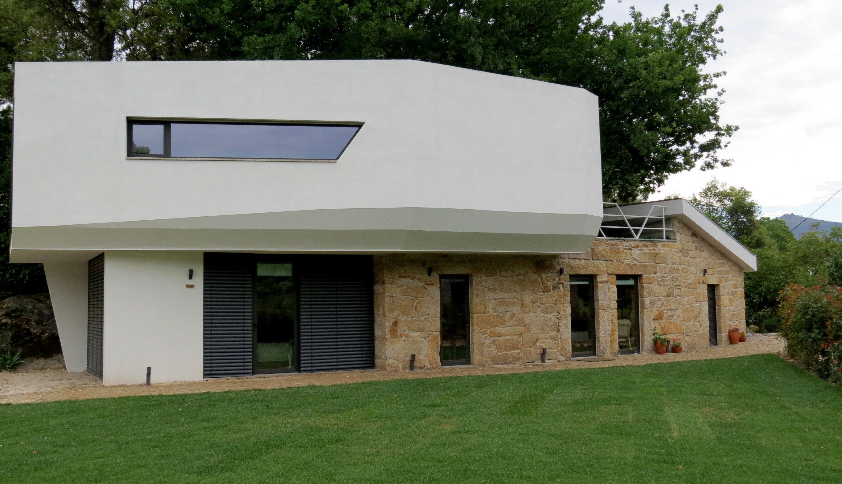 A modern two-story house with a flat roof, large windows, and a stone facade.