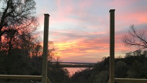 A deck with two Adirondack chairs overlooking a lake during sunset. - Clermont Bluffs B&B (Natchez)