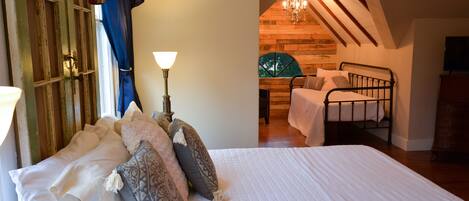 A bedroom with a large bed, a nightstand, a lamp, and a view of a dining area with a chandelier.