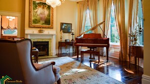 A grand living room with a grand piano, a fireplace, and a chandelier. - Clermont Bluffs B&B (Natchez)