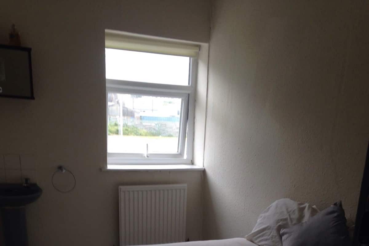 A bedroom with a bed, a window, a radiator, and a sink.