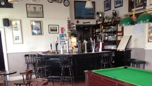 Et område med bar, hvor der er træborde og stole, et billardbord og forskellige billeder på væggene.
