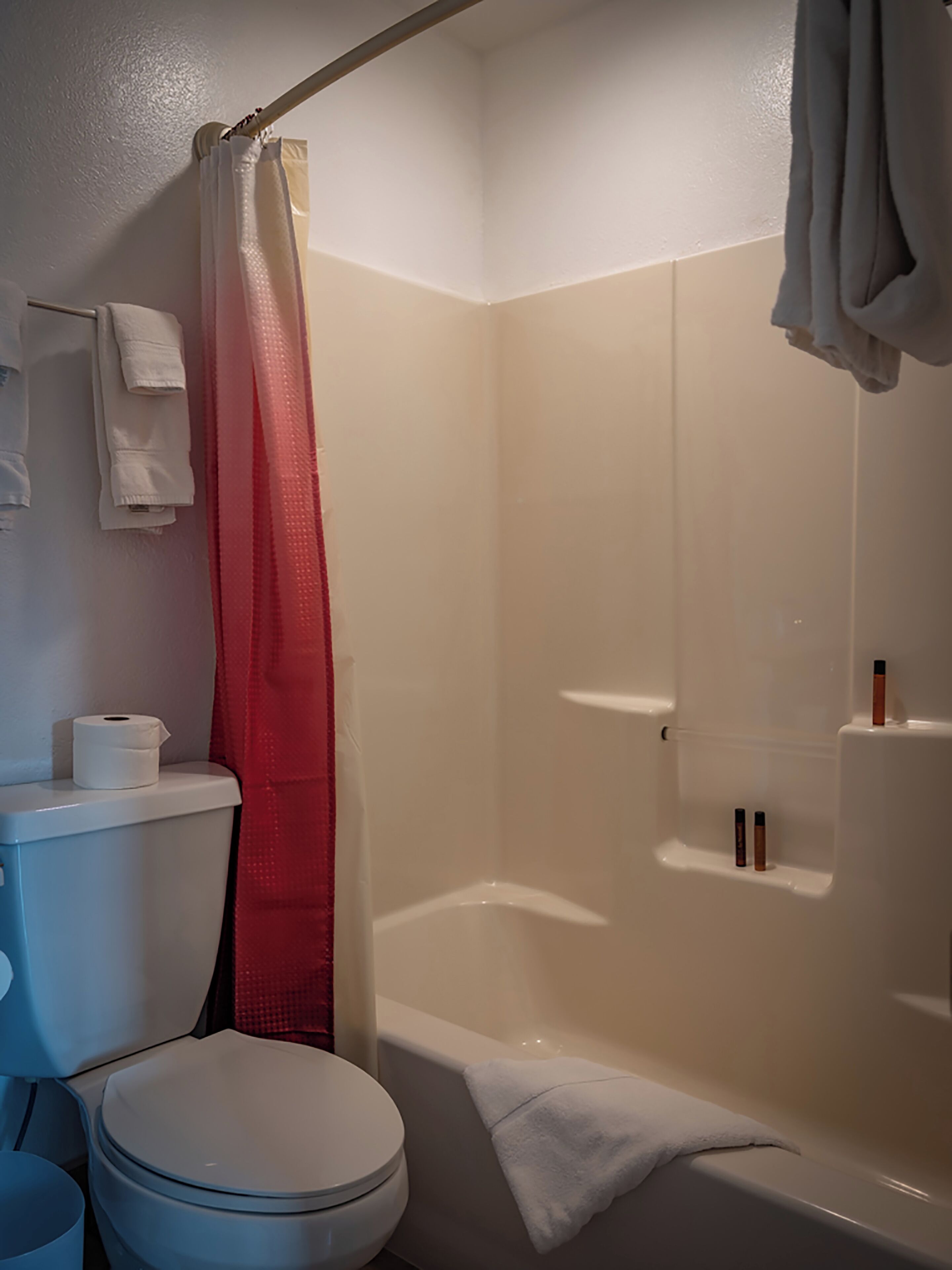 A bathroom with a toilet, a shower curtain, a bathtub, and a towel rack.